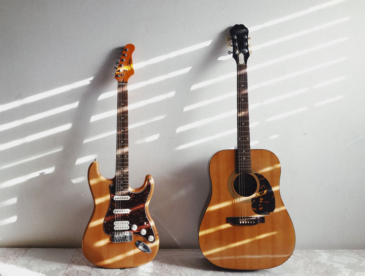 A minimalist scene featuring an acoustic and electric guitar against a white wall, perfect for music enthusiasts.